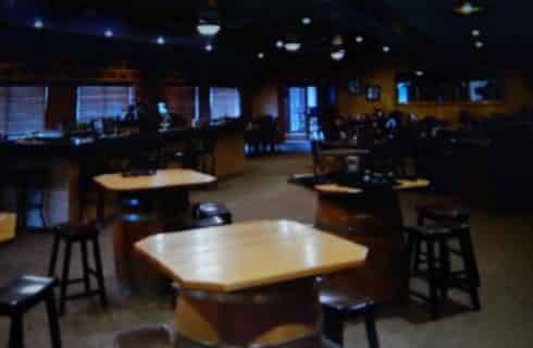 Inside of a restaurant with wooden tables and black bar stools