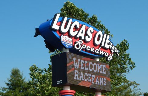 Large sign showing Lucas Oil Speedway, Welcome Race Fans with green tree in background