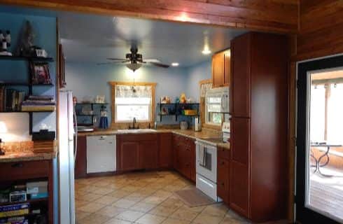 Kitchen with tan tiled flooring, dark wooden cabinets, white appliances, and blue walls