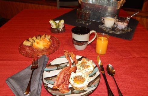Sausage egg cups and bacon served on a plate decorated with fish on a red tablecloth with coffee and orange juice