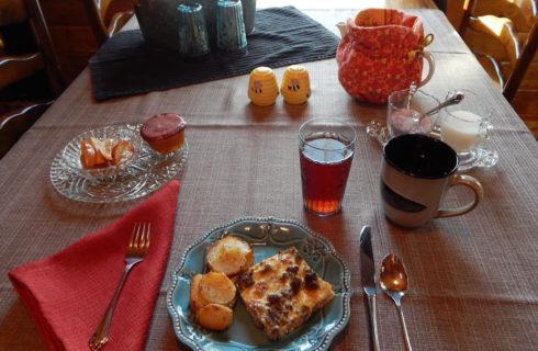 Egg and sausage casserole with fried potatoes on a blue plate resting on tablecloth with folded red napkin, juice, and coffee
