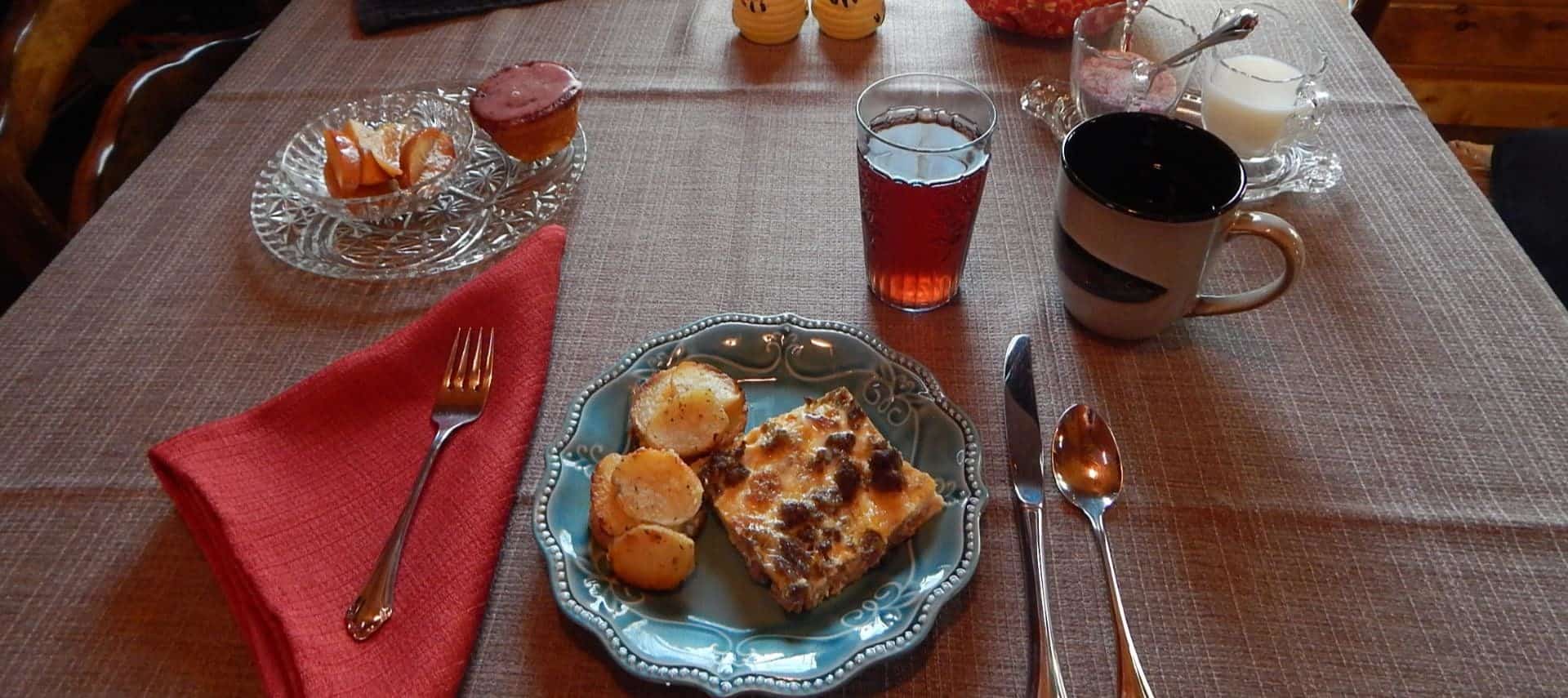 Egg and sausage casserole with fried potatoes on a blue plate resting on tablecloth with folded red napkin, juice, and coffee
