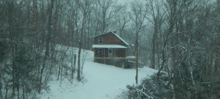 Brown cabin in the woods surrounded by trees and snow