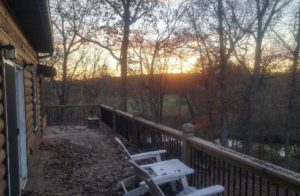 Exterior view of the cabin standing on the deck looking out to the river, trees and setting sun